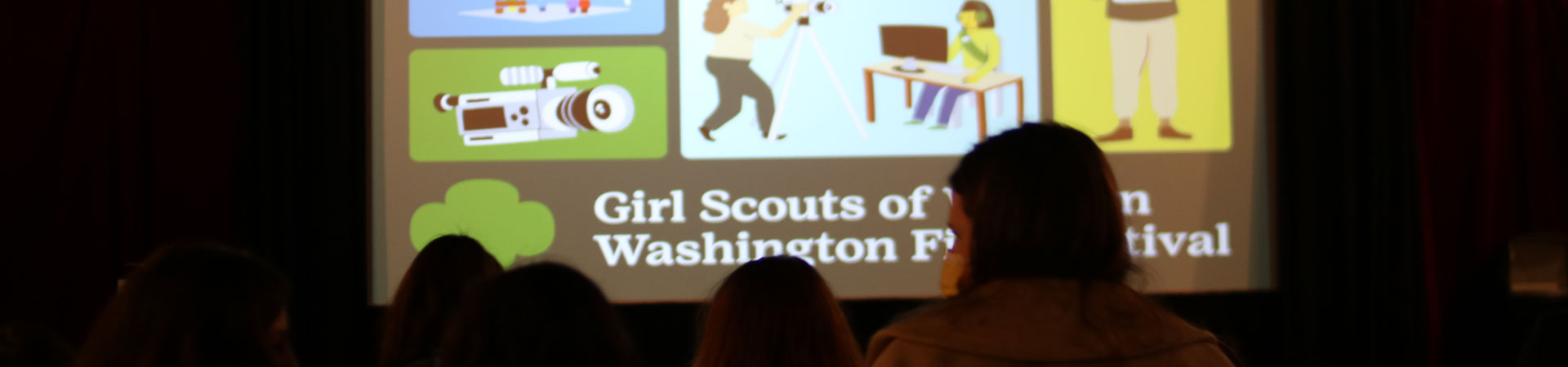  A theater is filled with seated movie-goers. There is a movie screen showing a still of various illustrations of Girl Scouts and filmmaking equipment and the words, "Girl Scouts of Western Washington Film Festival."  