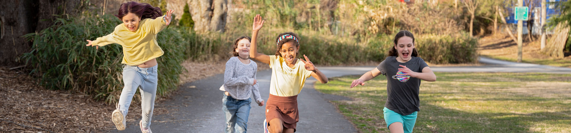  Four Girl Scouts running and jumping down a tree-lined path. 