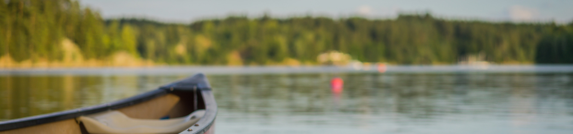  A close up of the tip of a canoe with a tree-lined lake blurred in the background. 