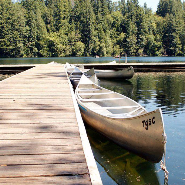 Two canoes next to a dock on a lake surrounded by evergreen trees at Girl Scout camp.