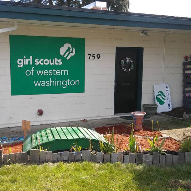 Headline reads, "Oak Harbor Girl Scout House - Est. 1956" with an illustrated bridge crossing a stream set against a brown background.