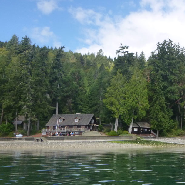 A large wooden structure on the shore of a lake surrounded by evergreen trees at Girl Scout camp Robbinswold.