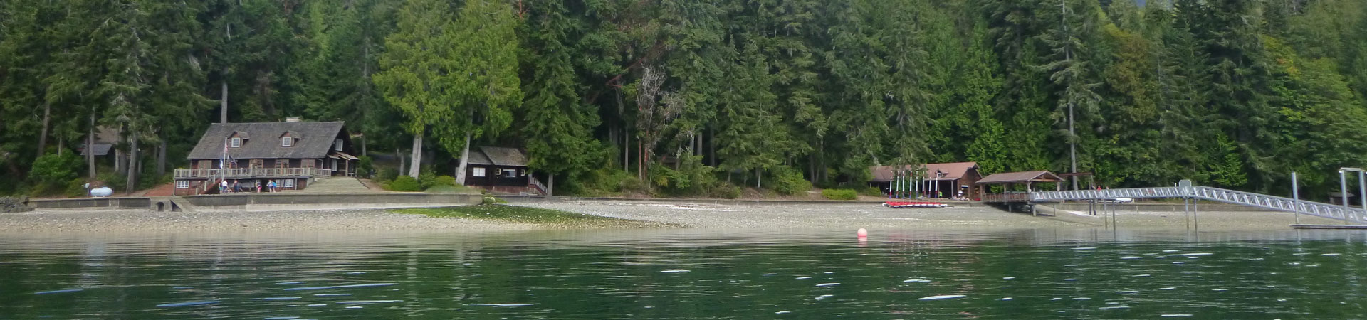  Image Description: Three lodges of varying sizes located on a rocky shore. There is a dock extending over the water and evergreen trees in the background. 