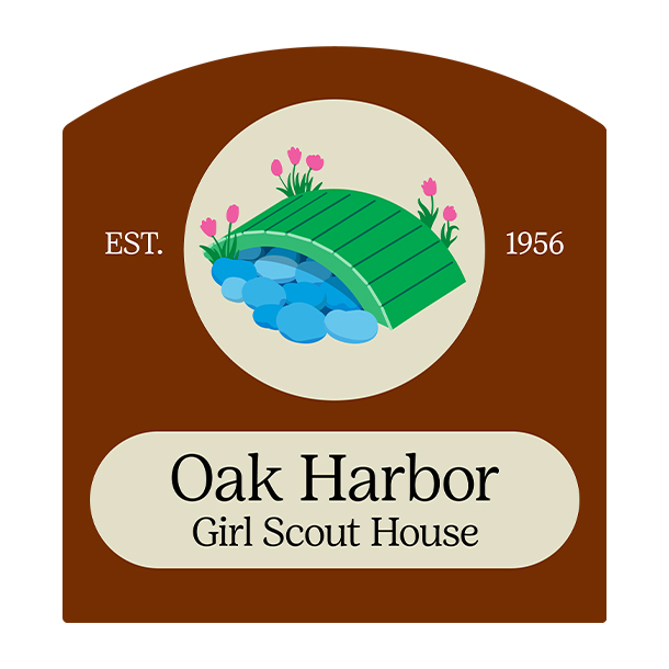 An exterior view of the Oak Harbor Girl Scout house. It is a cream-colored building with a dark door and a green and white sign that reads, "Girl Scouts of Western Washington." 