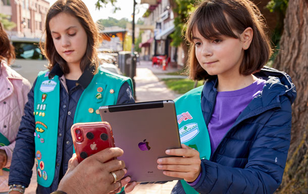 Two Girl Scouts in green vests process a cookie transaction on an iPad.