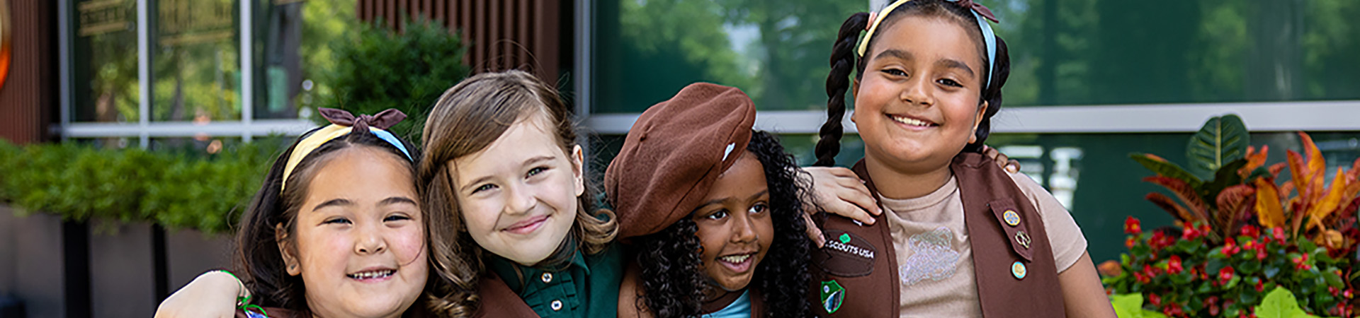  A close up of an iphone. On the screen, two Girl Scouts standing outside are holding boxes of Girl Scout Cookies. They are wearing face masks and are dressed in pink and purple. 