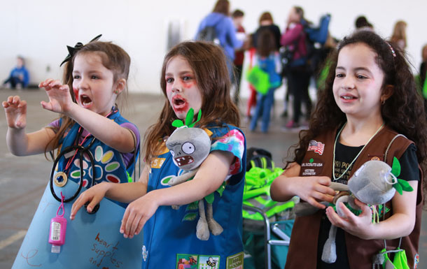 Three Girl Scouts wearing blue and brown Girl Scout vests with their faces painted to look like zombies.