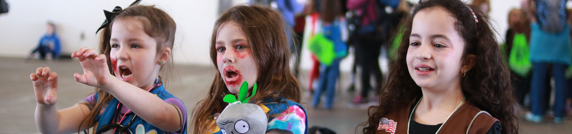  Three Girl Scouts wearing blue and brown Girl Scout vests with their faces painted to look like zombies. 