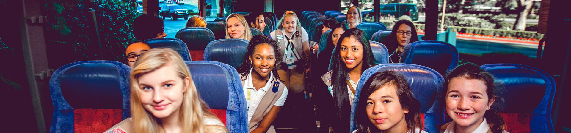  A group of Girl Scouts in Girl Scout uniforms on a bus with blue seats.  