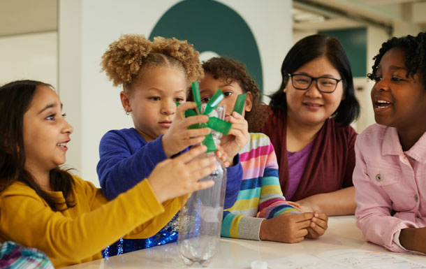 A group of Girl Scouts build a science experiment with a bottle while sitting together at a table.