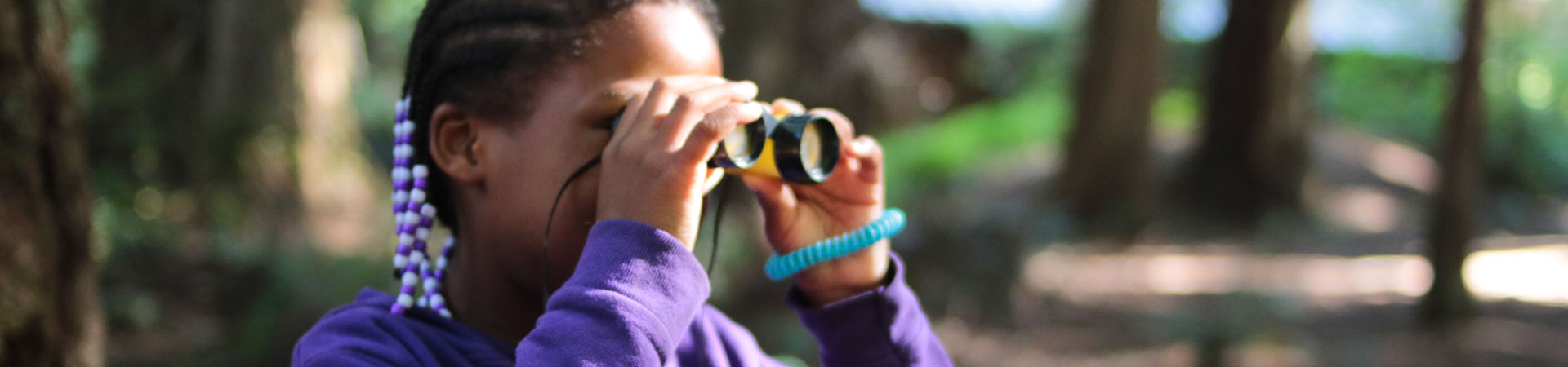  A Girl Scout wearing a purple sweatshirt looks out of pair of binoculars. 