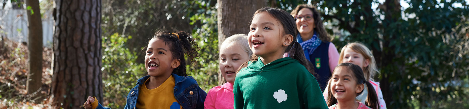  group of daisy girl scouts in vest and apron uniform hugging and smiling outside 