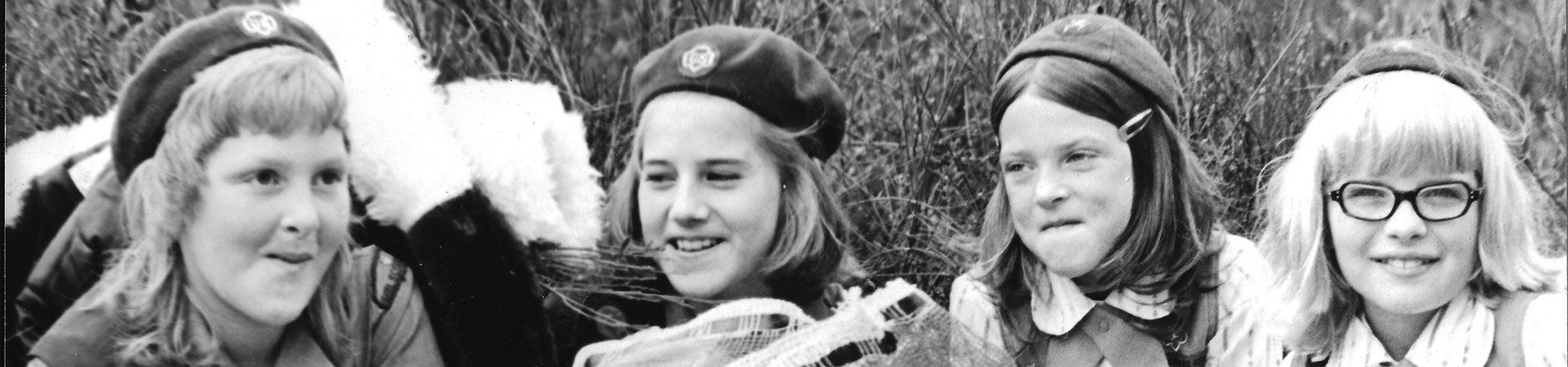  Image Description: A vintage, black and white photograph of four Girl Scouts sitting in a field. They are wearing Girl Scout apparel. 