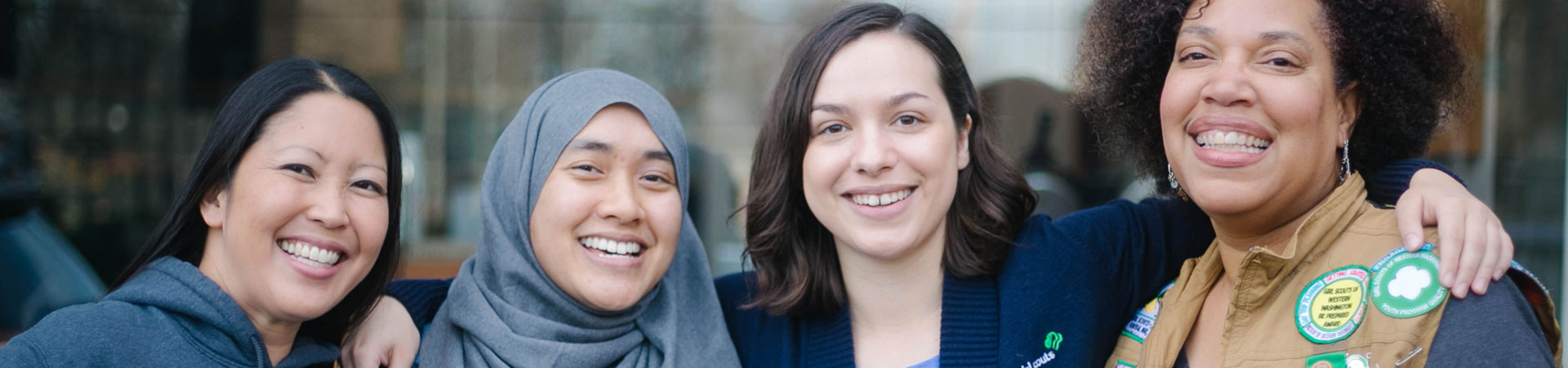  Four Girl Scout staff of various ethnic and cultural backgrounds stand together smiling. 