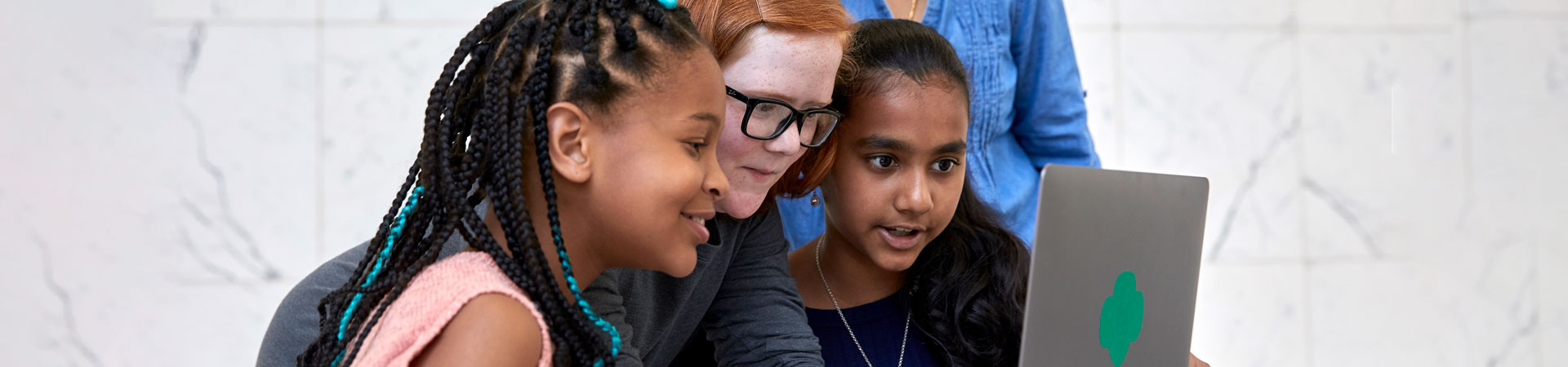  Three Girl Scouts looking at the screen of a silver laptop with a green trefoil.  
