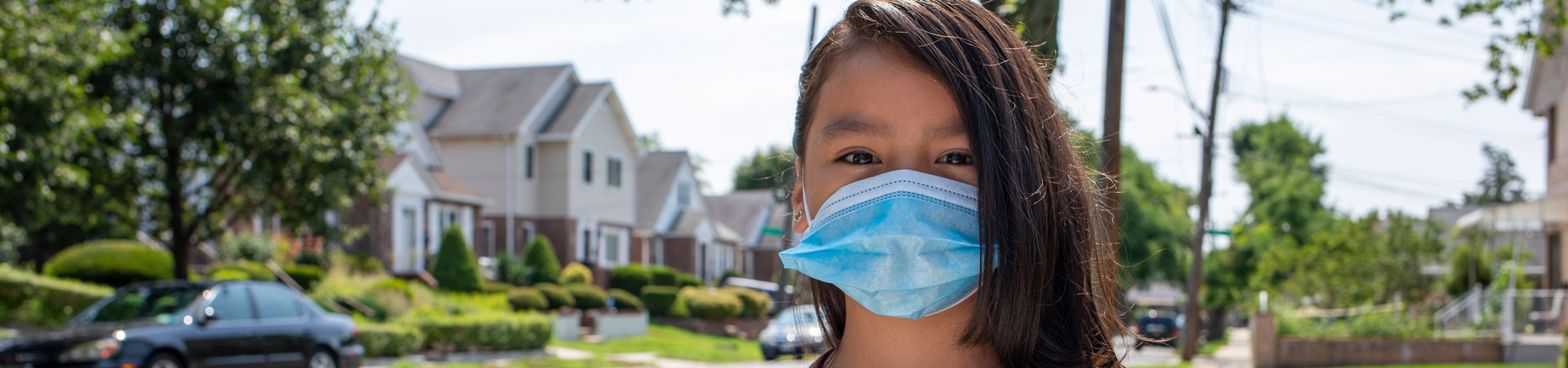  A Girl Scout standing on the sidewalk wearing a face mask. 