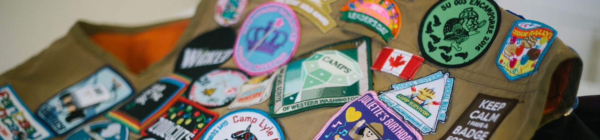  A close up of a khaki-colored Girl Scout vest decorated in a variety of colorful badges. 