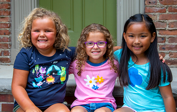 Girl Scout Daisies site together smiling in front of a brick building.