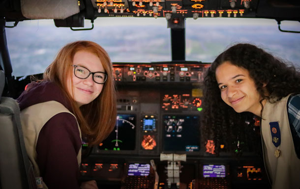 Two Girl Scouts sitting at the control panel inside an airplane.