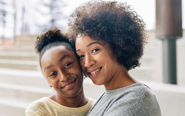 An adult volunteer and youth Girl Scout are smiling cheek to cheek. They are outside and there are stairs in the background.