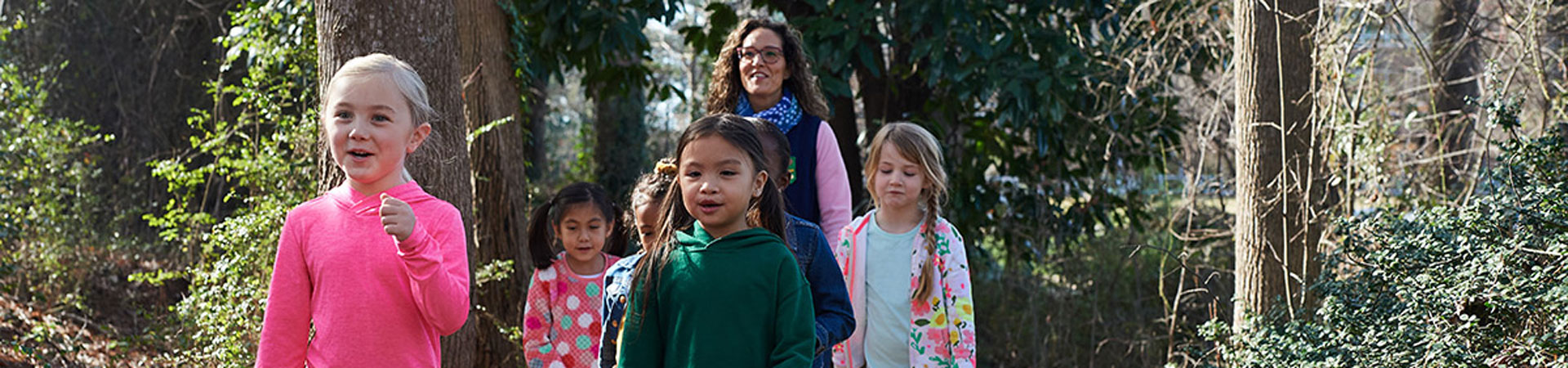  A group of Girl Scouts and an adult volunteer hike through the woods. 