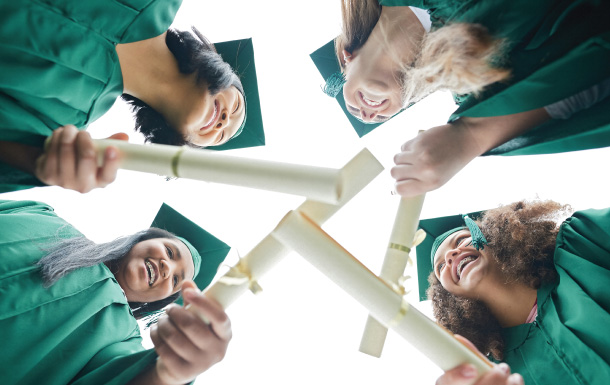 Group of older Girl Scouts wearing green graduation caps and gowns stand in a circle holding their high school diplomas.