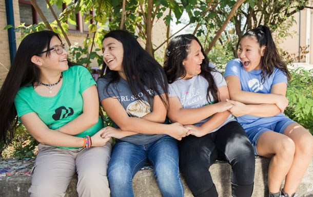 Four adult Girl Scout members sitting outdoors with their arms crossed, holding each other's hands.