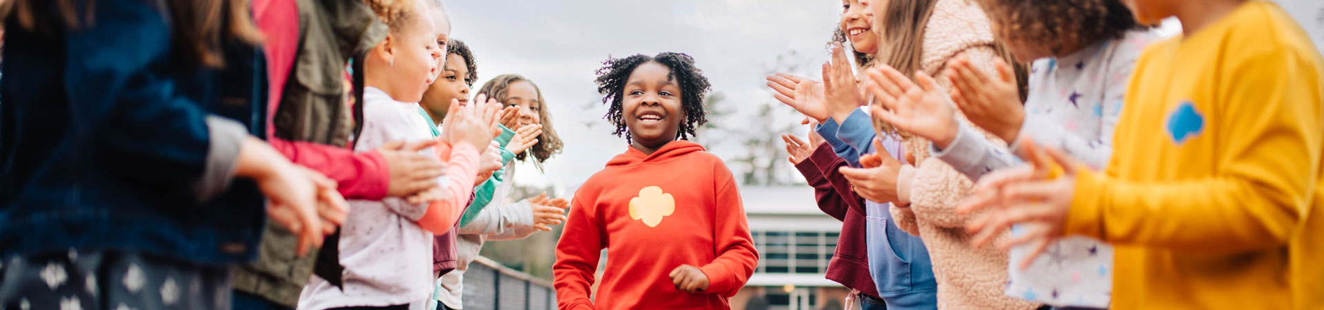  An Individually Registered Member Girl Scout runs on a track while a crowd of Girl Scouts cheers them on from the sidelines. 