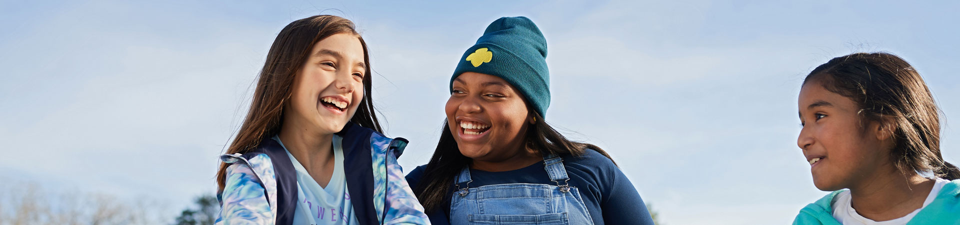  Three smiling Girl Scouts sitting in the grass on a blue-skied day. 