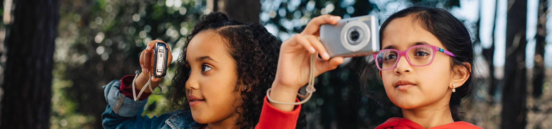  Two Girl Scouts taking photos in a wooded recreation area.  