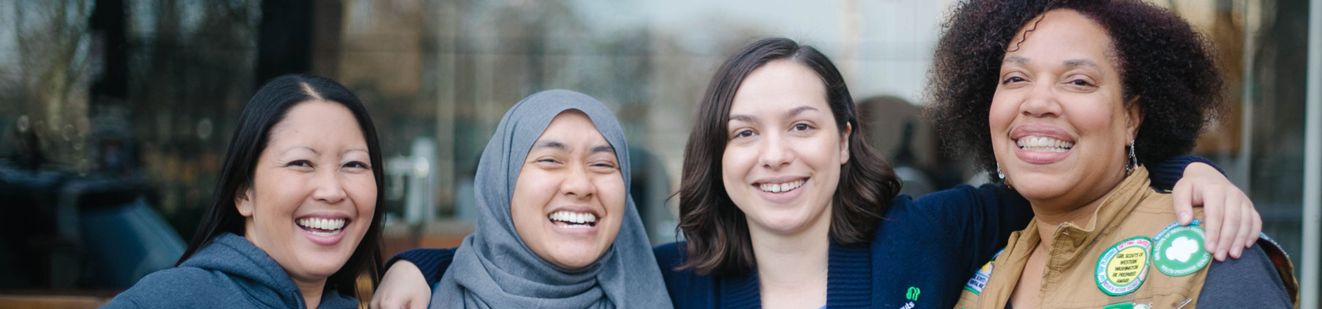  Four adult volunteers stand arm in arm smiling. 