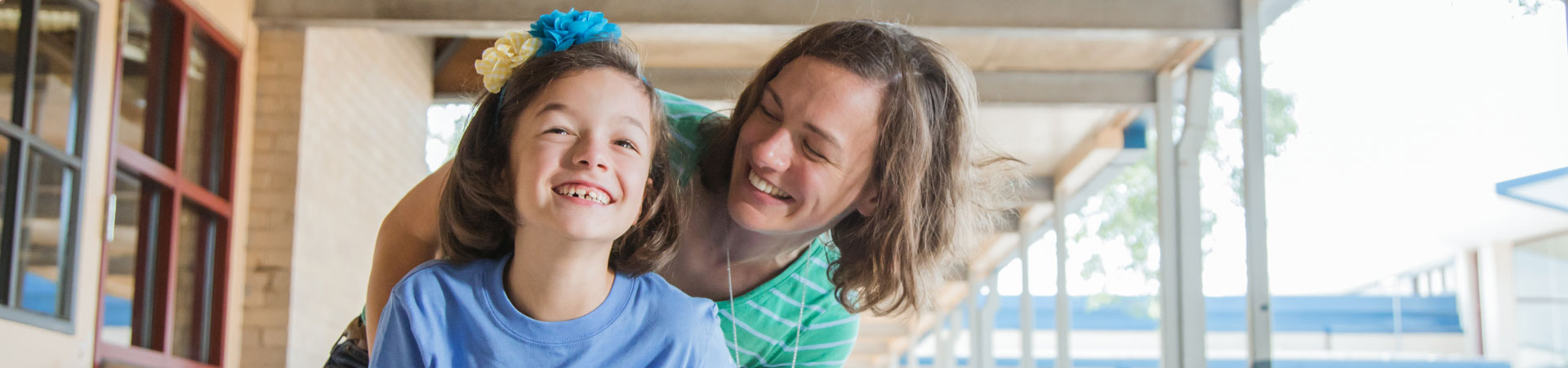  A mom in a Green shirt hugs a Girl Scout wearing a blue shirt from behind, both smiling. 
