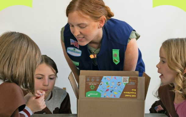 Three Girl Scouts outdoors counting money and taking notes. An adult volunteer supervises.