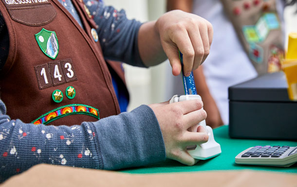 A close up of a Girl Scout's hands inserting a credit card into a card reader.