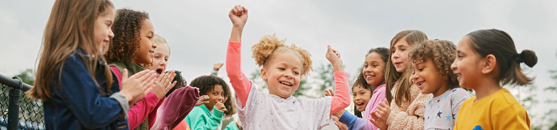  Girl Scout with pigtails raises arms as she runs through a crowd of kids outside on a running track. 